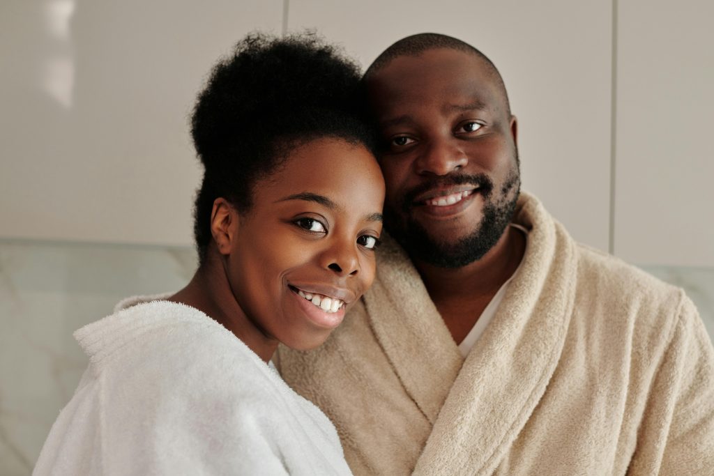 Smiling African couple wearing bathrobes, sharing a loving moment indoors.