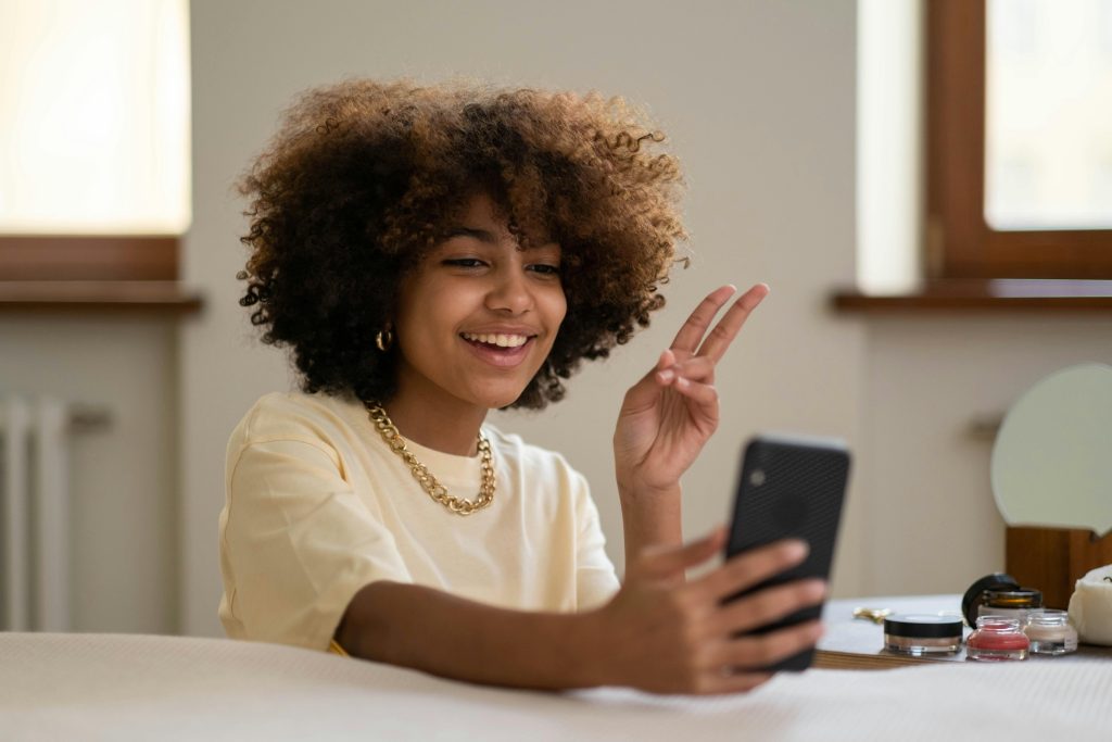 A joyful woman with afro hair takes a selfie indoors, showcasing self-love.