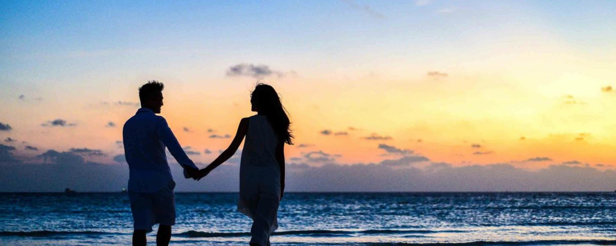 pexels-photo-1024960-1024960 A romantic couple walks hand in hand on a tropical beach at sunset, enjoying a serene moment together.